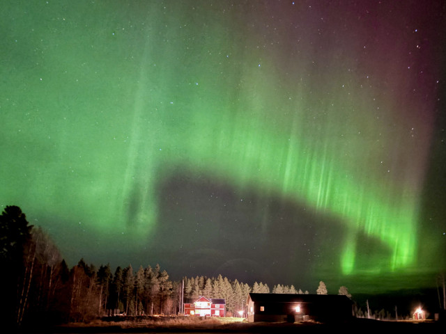 A red and green aurora arc above a farm house.