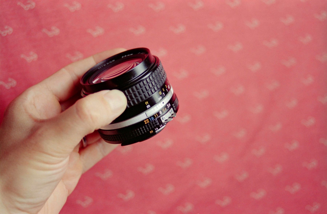 Lens in hand with the glass pointing up on a pink textured background