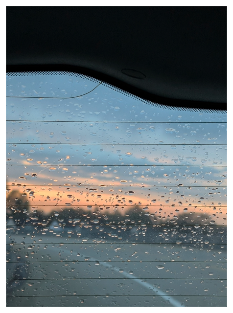 sunset during a light rain. view through a car's rear window of a freeway overpass and a treeline in the mid-distance at sunset.