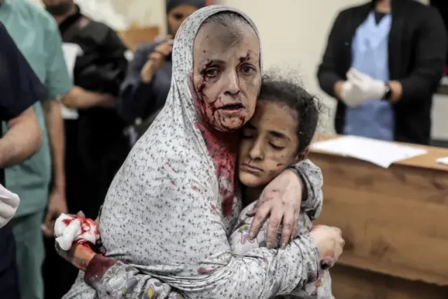 Injured woman covered in dust and blood hugging her bleeding daughter in a hospital, November 15, 2023