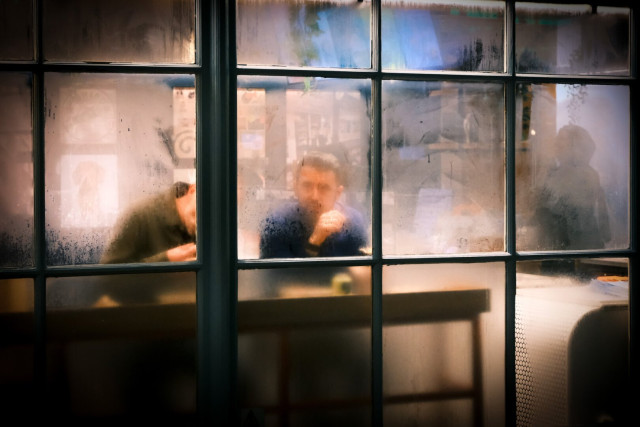 A cinematic colour photo of two men sitting by the window of a London restaurant. The window is covered in condensation, giving the scene a misty look.