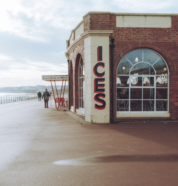 A elderly gentleman makes his way towards the doorway of a seafront cafe