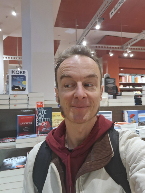 Der Autos macht ein Selfie vor seinem Buch auf einer Displayinsel voller Bücher.