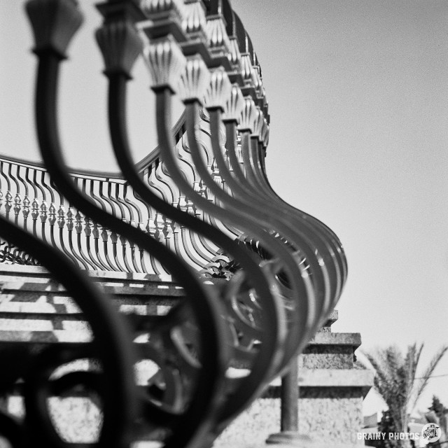 A black-and-white film photograph showing the ornate steelwork balustrade on the spiral staircase