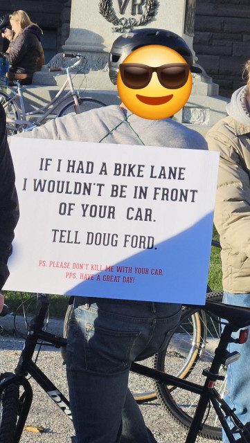 Sign on a person's back that reads:

"If I had a bike lane I wouldn't be in front of your car. Tell Doug Ford."

"P.S. Please don't kill me with your car."

"PPS. Have a great day!"