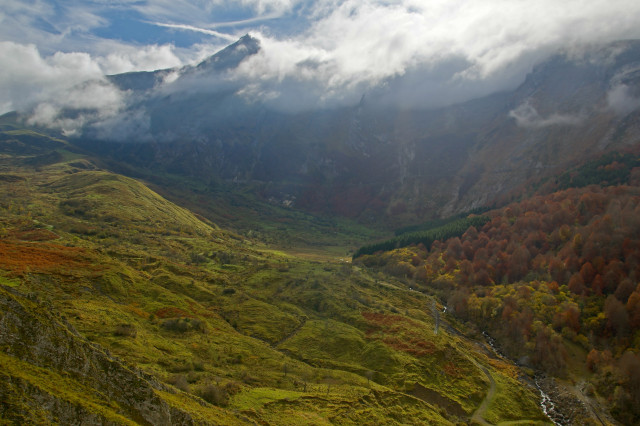 The view on Cirque du Litor from the road from Arbeost to Col du Soulor, today. A wide valley of green, red, and golden colors of prairies and trees, cliffs split by the road between soulor and aubisque, and the grand Gabizos peak tearing out cloud, some blue sky. Very intense, magical colors and lightning.