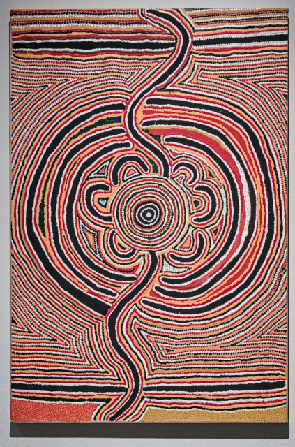 A color portrait photo of an acrylic on canvas geometric / abstract painting. It is made of of lines, circles, and arches. A black curvy line runs from top to bottom. Black, red, and white crescents are on the left and right. In the center are concentric circles of white, yellow, red, and black. There are straight horizontal lines of the same colors top and bottom. 