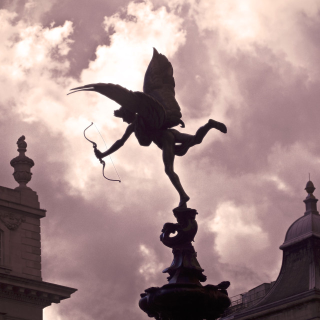 The statue of Anteros at Piccadilly Circus, London. A winged youth balances on top of a fountain, clutching a bow, against a cloudy, purplish sky.