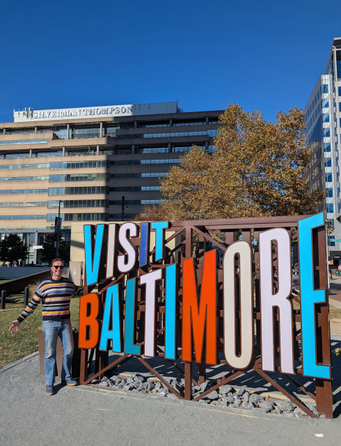 Me wearing a striped sweater next to the 'Visit Baltimore' sign