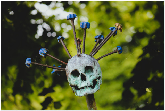 Skulptur eines Totenschädels mit mehreren Quirlen, die wie abstehende Haare aus dem Schädel emporragen.