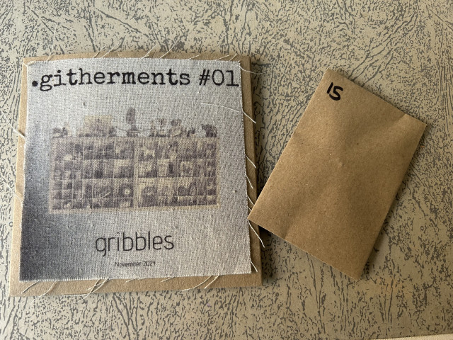 Photo of the cover of githerments - it's a knick-knack shelf colourised in faded sepia with the title 'githerments #1' above it in a typewriter font and gribbles below. It is printed on a calico square, which is fraying round the edges and stuck to the front of the brown cardboard CD case. Next to it is a small brown envelope with the number 15 written on it.