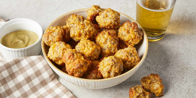 An image I found via a Google search that shows a ceramic bowl that is filled with sausage balls. There is another smaller bowl with some kind of dipping sauce maybe and a glass in the background with something filling it halfway. 