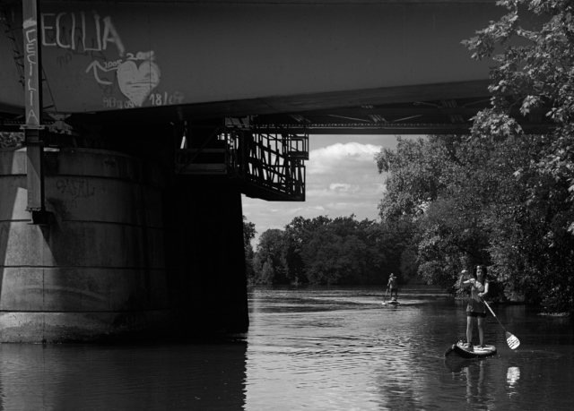 Black and white daylight photo.
Highly contrasted characters made of flesh, concrete, foliage or flowing water trying to adapt to a convoluted scenario involving a mysterious Cecilia.
The bridge framing the adventurous couple over the river is most probably there to distract us from the main plot.