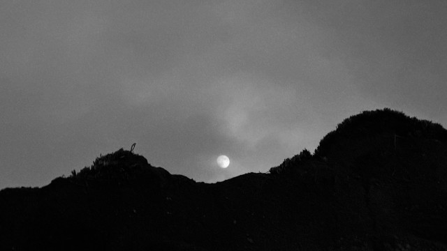 moon rising behind dark hills and through clouds 