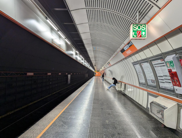 U-Bahnstation in Wien mit den typischen Designelementen wie weisse Panele mit und ohne Löcher, Ecken und Tafeln in der Linienfarbe und wunderbarer Helvetica-Typographie. Die Stationsrückwand ist halbrund gebogen, die Wand auf der Gleisseite liegt im Dunkeln.