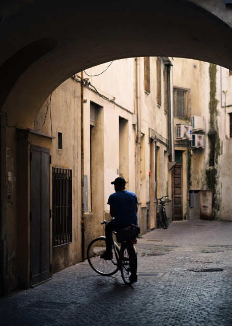 A man on a bicycle seems to be waiting for something near an entrance door in a side alley.