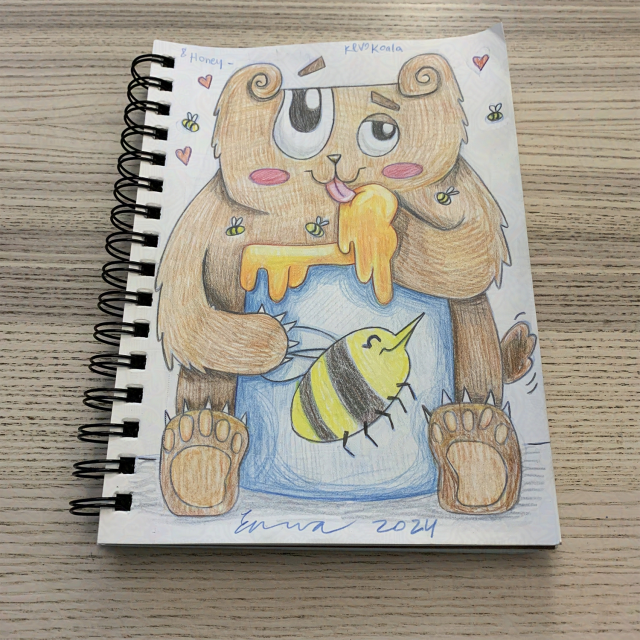 sketchbook resting on a pale wooden surface. drawing of a happy bear licking honey off of his paw. the jar is blue with a large smiling bee on it and honey on the rim. there are small bees and hearts around the bear. there is a bold signature and year at the bottom."8 honey -" and "kevokoala" is at the top.