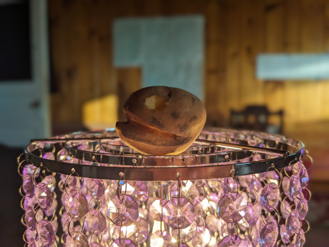 A potato that looks suspiciously like video game character Pac-Man resting atop a purple sparkly lamp.