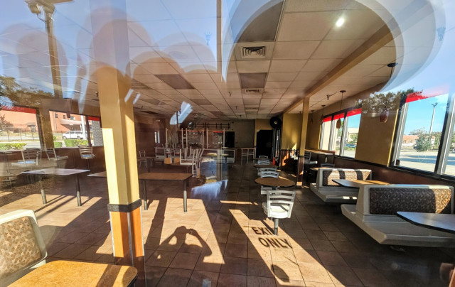 Inside view of an abandoned Burger King restaurant. Shadows from the many windows stretch across the inside, left exactly as it was on the final day in operation, almost like a tomb.