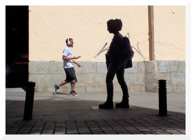 A mixture of shadows and lights. In the foreground, in shadow, is the silhouette of the statue ‘Young Girl Walking’, located in the Plaza de San Idelfonso in Madrid. In the background, in the light, a man with headphones walks towards it.
----
Mezcla de sombras y luces. En primer término, en sombra, está la silueta de la estatua ‘Joven caminando’, situada en la plaza de San Idelfonso de Madrid. Al fondo, en la luz, un hombre con auriculares camina hacia ella.