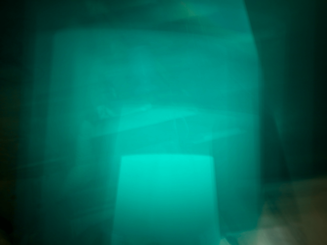 Multi-exposure photo of a mint green lampshade (with the light on) most prominently featured in the bottom center of the frame.