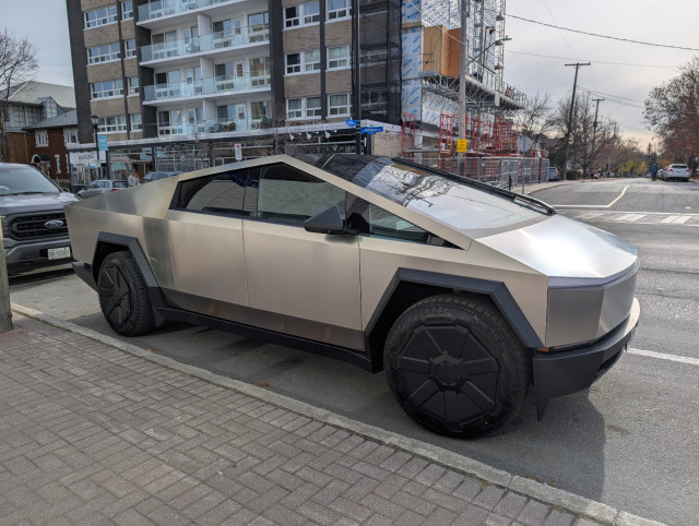 A Tesla CyberTruck, parked on a city street.  It looks like an enlarged toy.