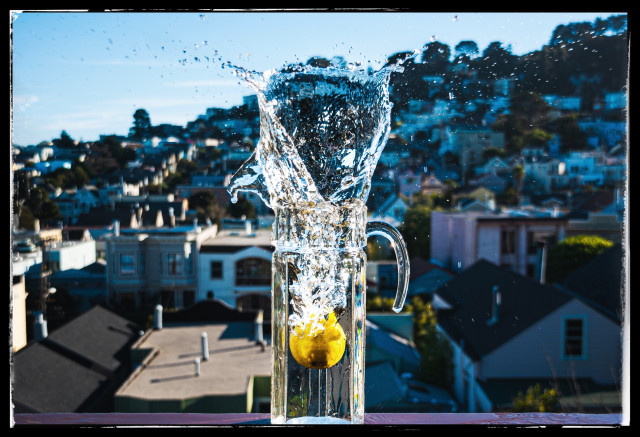 This is a stupid picture of a lemon, dropped from very high, into a narrow water pitcher that is sitting on the railing of my 3rd story deck in San Francisco. The lemon hits the water and plunges downward, creating a tall calla lily shaped, sparkly, upward splash.

Over a dozen lemons were lost in this experiment. Most landed on the deck below. A few hit the ground 35 feet down. Only one hit the mark.

It's fucking hard dropping a lemon using a long tongs with one hand while pointing a camera with the other. It takes aim, timing, focus, and pot. Ansel Adams could never...