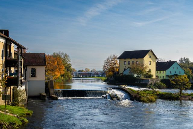 Blick auf einen Fluss mit Wehr, städtisch. Links Häuser, rechts Häuser, blauer Himmel, Herbststimmung.