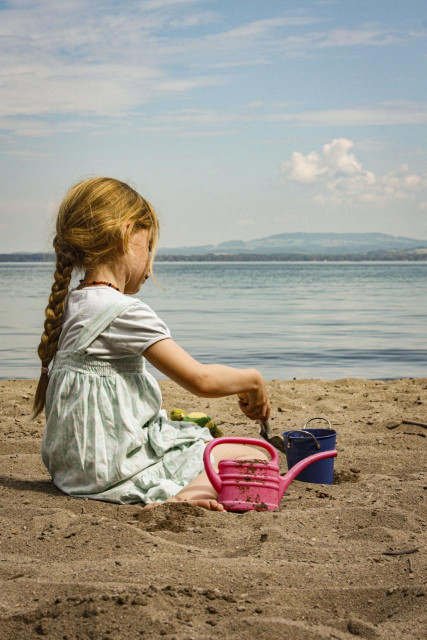 Blondes Mädchen (ja, K2) spielt am Strand mit Förmchen, Eimerchen und Schäufelchen