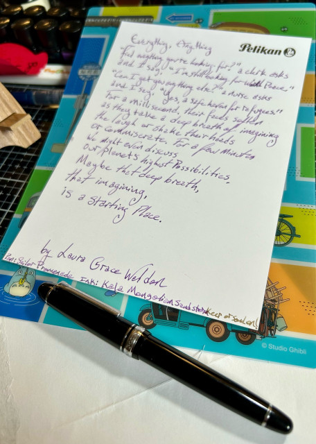 A crisp, white sheet of paper made by Pelikan (logo to upper right) sits a top a Totoro themed writing board. A poem by Laura Grace Weldon is handwritten on the paper in a lovely purple ink. Below the author’s name is a line sharing the pen and ink used (pen: Sailor Promenade, ink: Kala Mongolian Sandstorm). At the bottom, below the paper sits a black fountain pen with its cap on.