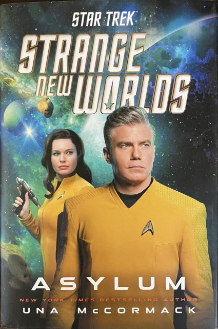 Cover of Strange New Worlds novel Asylum (2024) by Una McCormack, showing Pike looking out of frame and Una with a phaser in her right hand looking in the same direction. In the background on the left is a bluish green nebula with what looks like a bluish green planet, a few asteroids, and a bright star.