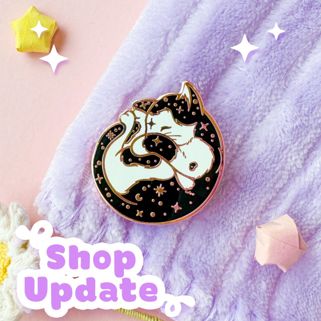 A photo of a rose gold enamel pin of a tuxedo cat curled up like a little croissant, it's fur is scattered with stars.