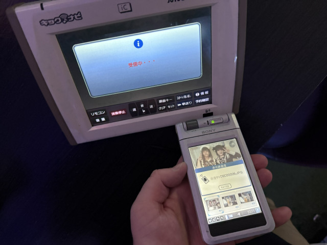 A Sony Clie in front of a karaoke remote with the Clie showing the PalmOS beaming dialog and the karaoke control showing a receiving message