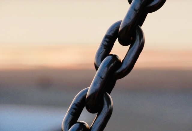 Eine Nahaufnahme eines Metallkettenglieds vor einem verschwommenen Hintergrund mit sanften Farben, die typisch für einen Sonnenuntergang sind. 

A close-up of a metal chain link against a blurred background, featuring soft colors typical of a sunset.