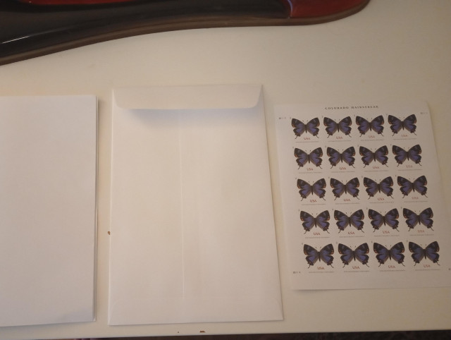 the 8.5x5.5 inch booklet next to a 9x6 inch catalog envelope, and a sheet of postage stamps. the stamps say "non-machinable surcharge" on them and have pictures of butterflies.