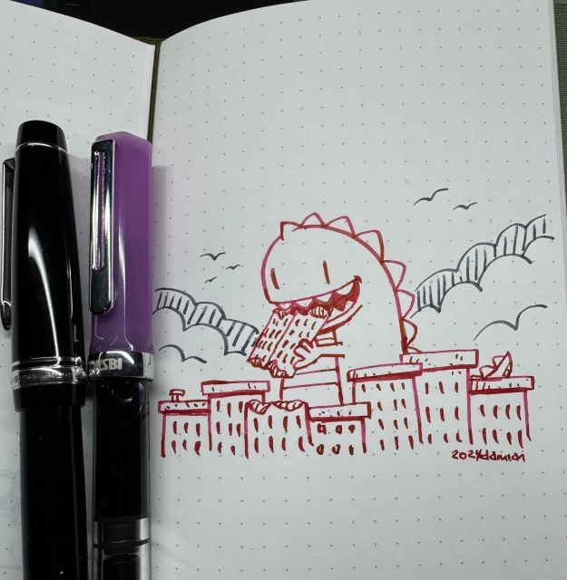 Dotted notebook page with two fountain pens sitting to the left. In red ink a Zilla is eating the upper part of a building he broke off, while surrounded by other buildings in a cityscape. Behind in grey ink is some smoke rising on either side and some birds in the distant sky.