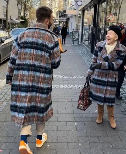 a young man and an old woman meet on the street expressing their surprise that they are wearing the same eccentric coat