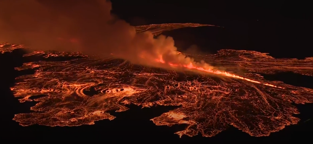 A long crack with lava flowing on all sides, almost looks like a train of fire going through a field.