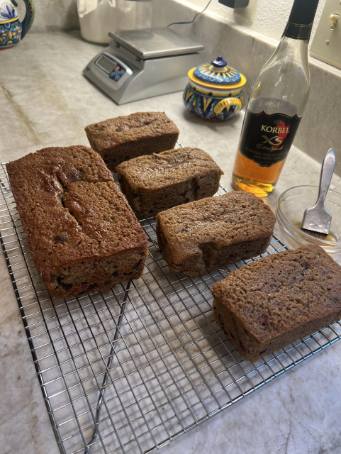 Four loaves of fruitcake on a cooling rack. A bottle of brandy and a brush for brushing the warm cakes