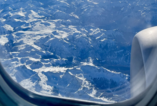 View of snowy mountains out the window of a plane. 