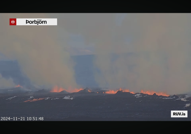 Screenshot from Rùv livestream, camera Þorbjörn, a long row of fires, lots of smoke in the air, also smoke coming from patches on the ground almost looking a bit like snow.