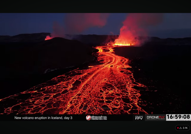 Screenshot from livestream. A huge lavariver flowing while making an intricate pattern, in the very back fountains and pink smoke. 