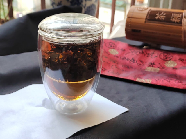 This is the tea while brewing.  And here's where I came to the conclusion that I may have used too few leaves.  The leaves just aren't filling the basket, and usually when making fermented teas that basket is packed tight.

The error I made was that I used the loose leaves that had flaked off the chunk, so the density of tea was lower.  I selected a volume of tea leaves that would ordinarily have been that volume of densely-packed tea.

The result is what you see: a liquor that is a nice burnt umber in colour, but not the titular *black* that an aged, fermented tea should give on the first brew.

The scent was still nice.  It has a good earthy bouquet with a hint of something slightly fruity (almost orange-like) and just a touch of sharpness like a single curl of a citrus peel being added.