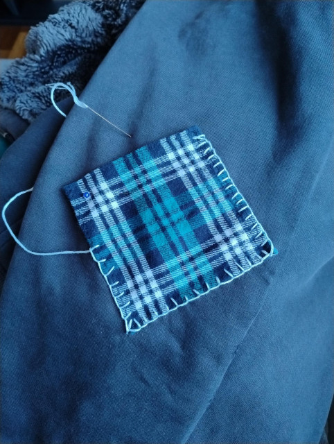 The image shows a patch being sewn onto a hoodie elbow, using a blanket stich. The stiching is a little bit uneven. It looks very 'homely'.