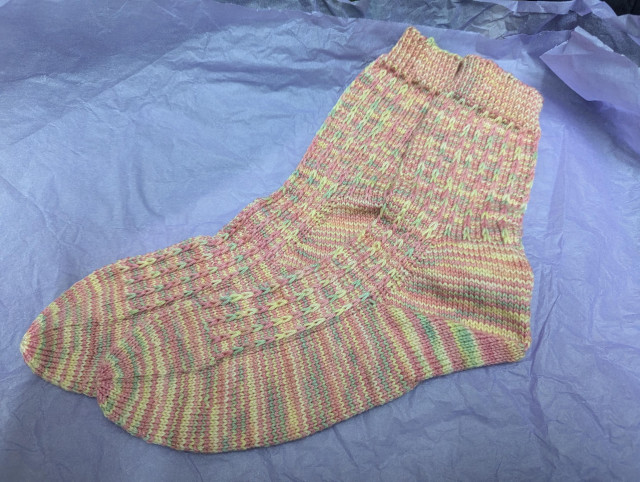 A pair of handknitted socks in pastel shades of pink, yellow and green