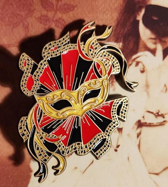 Masquerade mask enamel pin in gold black and red against a vintage photo of a woman in a Masquerade mask