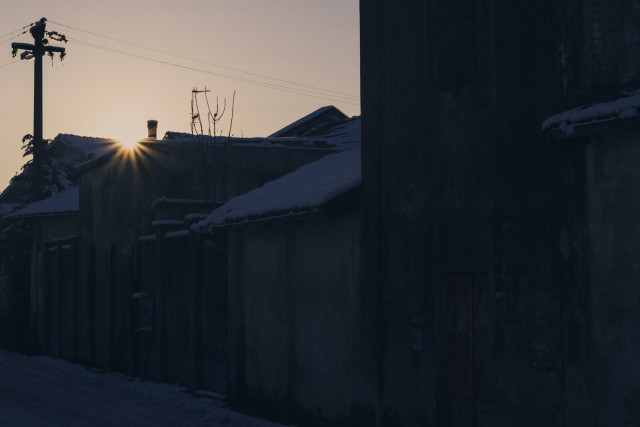 Photo of an old factory complex and the sun just popping out from behind the roofs