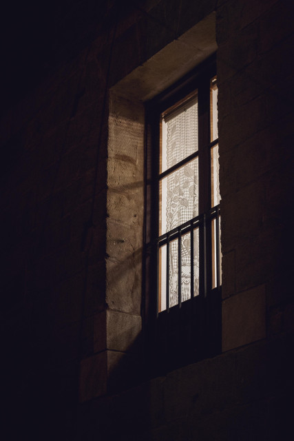 Se ve de forma perpendicular una ventana iluminada de noche. A su alrededor, oscuridad.