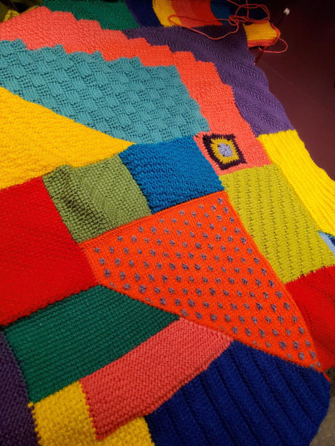 Multi-coloured and many textured afghan crochet project in progress, with hook and loose yarn visible near the top of the image