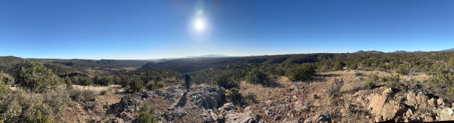 The New Mexico high desert under a blue, blue sky and a glowing sun. Mountains in the distance. Up close, piñon and scrub cedar spread over the rolling ridges and gorges. 